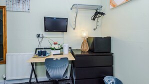 Une pièce de taille modeste, équipée d’un bureau, d’une chaise, d’une télévision et d’un petit réfrigérateur.