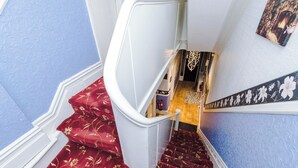 Un escalier dont les marches sont recouvertes d’une moquette rouge, menant à un palier.