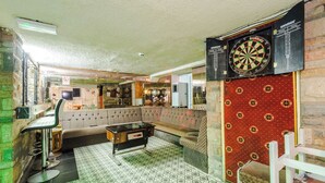 Une pièce comprenant un jeu de fléchettes, un canapé, un coin bar et un sol à motifs.
