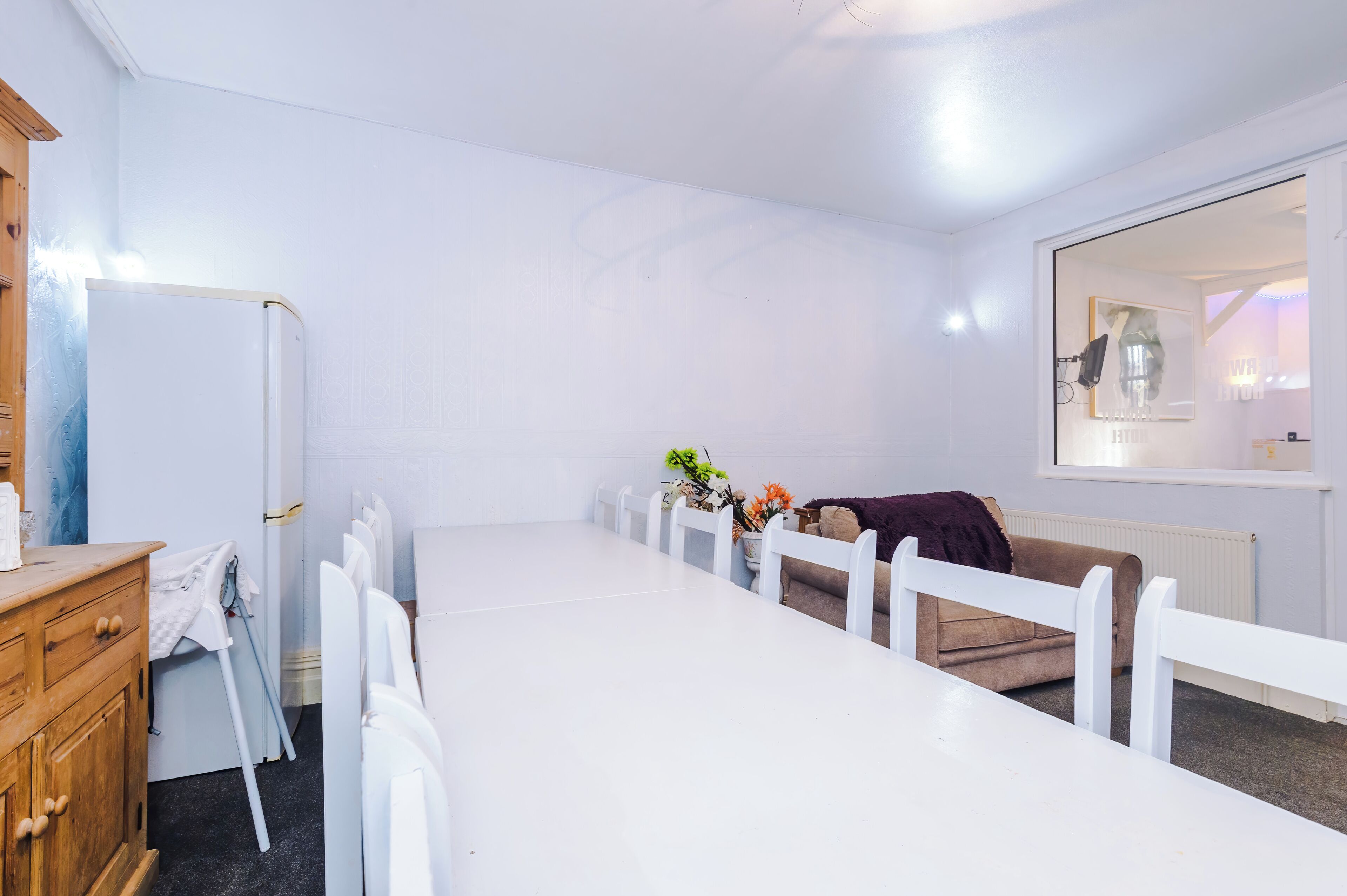 A room with a white table, chairs, a wooden dresser, and a window with a view of the outside.