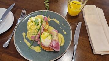 Um prato de ovos Benedict com presunto e molho holandês, um copo de suco de laranja e uma toalha de papel dobrada sobre uma mesa de madeira.
