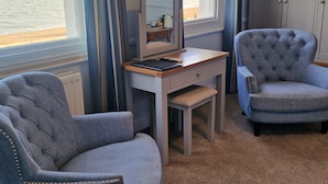 A room with two upholstered chairs, a small desk with a mirror, and a view of the sea through large windows. - Dunkerleys Hotel (Deal)