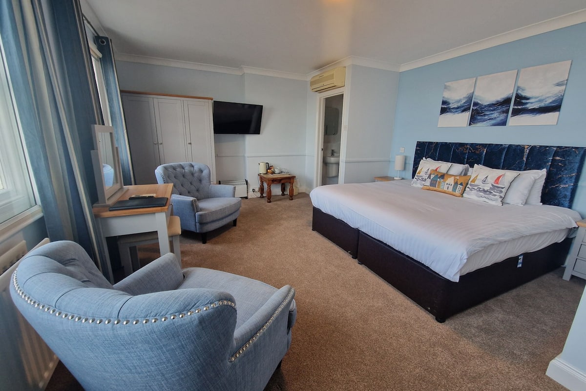 A hotel room with a bed, a desk, a chair, a TV, and artwork on the wall.