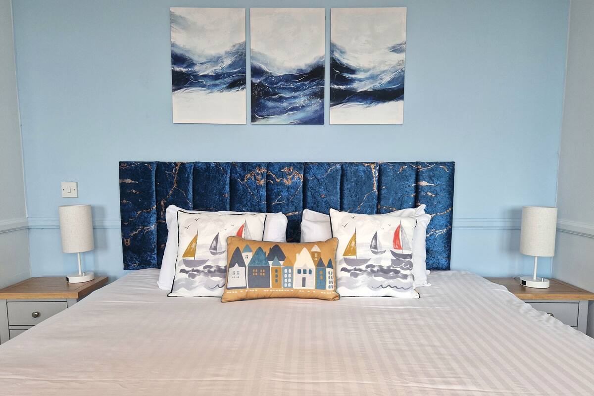 A bedroom with a large bed, a marble headboard, and three wall-mounted paintings.