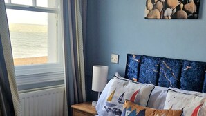 A bedroom with a bed, a nightstand, a lamp, a window with curtains, and a painting on the wall. - Dunkerleys Hotel (Deal)