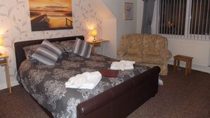 A bedroom with a large bed, a chair, a nightstand, and a painting on the wall. - Easton Court (Paignton)