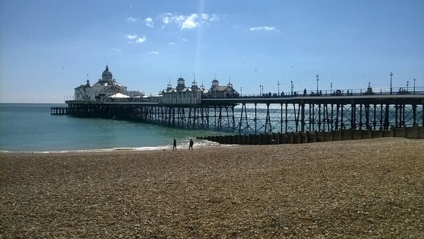 A pebbled beach with a pier extending into the sea, featuring a large building with a dome and several smaller structures. - Ebor Lodge (Eastbourne)