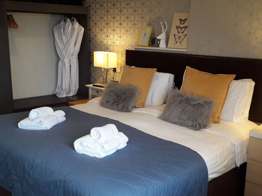 A hotel room with a large bed, two bedside tables, a nightstand, a robe hanging on the wall, and a patterned wallpaper.