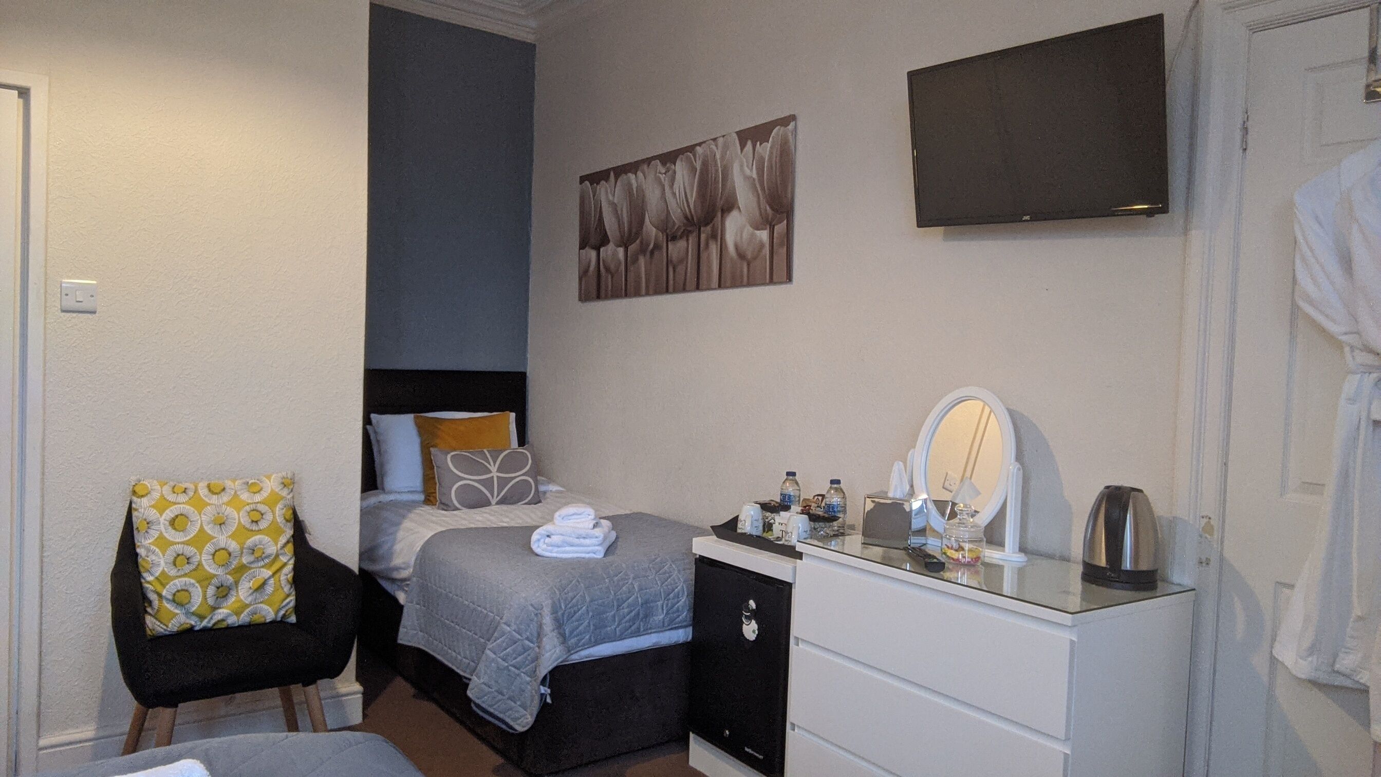 A bedroom with a bed, a chair, a dresser, a mirror, and a painting on the wall.