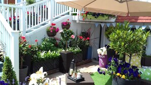 A balcony with potted plants, a wicker chair, and a small table with a candle and a vase. - Ebor Lodge (Eastbourne)