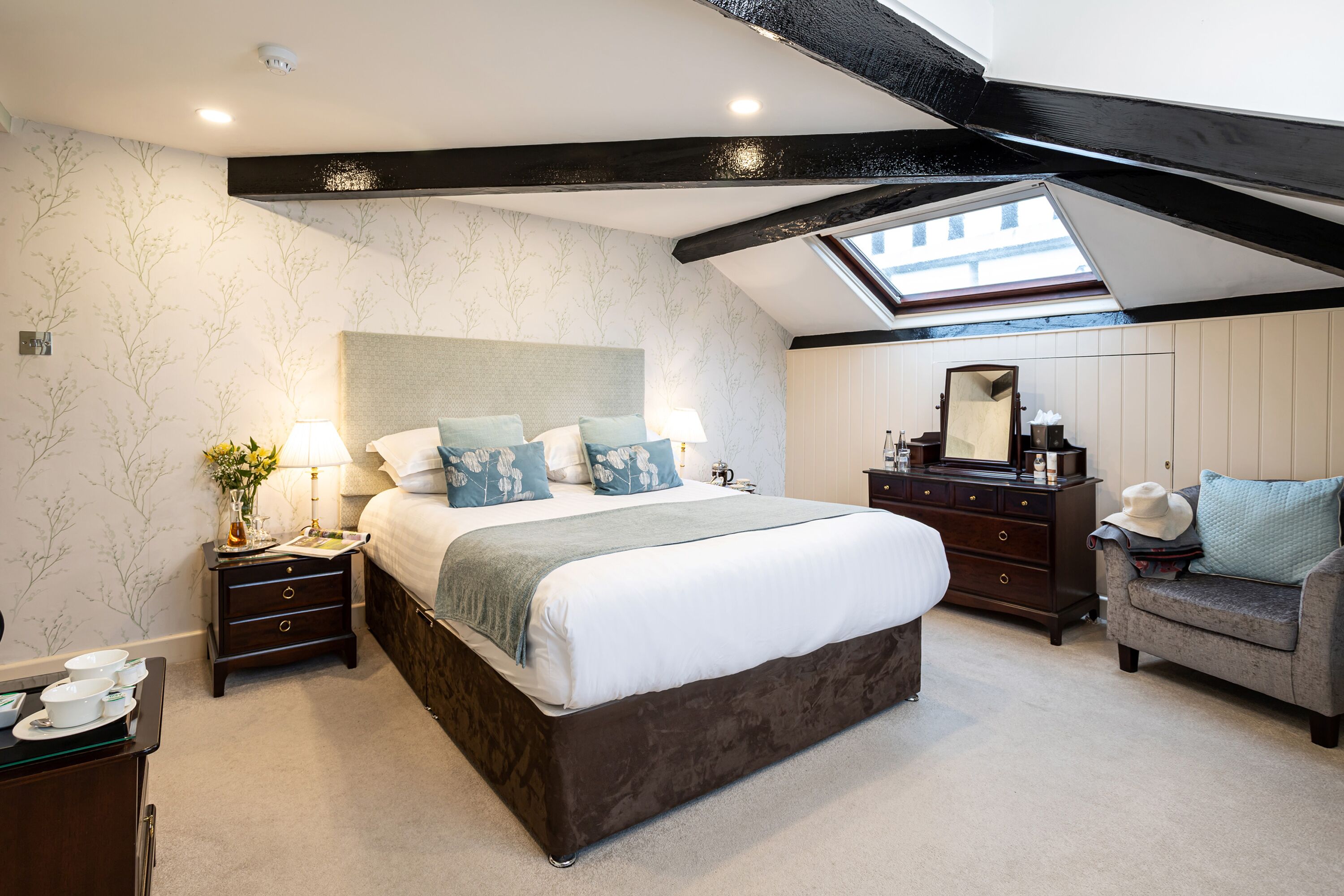A bedroom with a large bed, a nightstand, a dresser, a mirror, and a skylight.