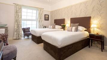 A hotel room with two beds, a sitting area with a chair, a small table, and a window with curtains.