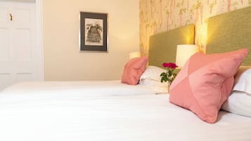Uma cama bem arrumada com lençóis brancos e almofadas cor-de-rosa, um quadro na parede e um abajur ao lado da cama.