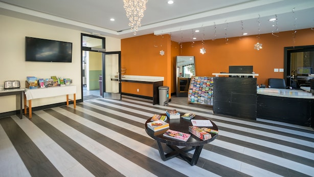 A reception area with a striped floor, a reception desk, a counter, a chandelier, and a wall-mounted TV. - Motel Capri (San Francisco)