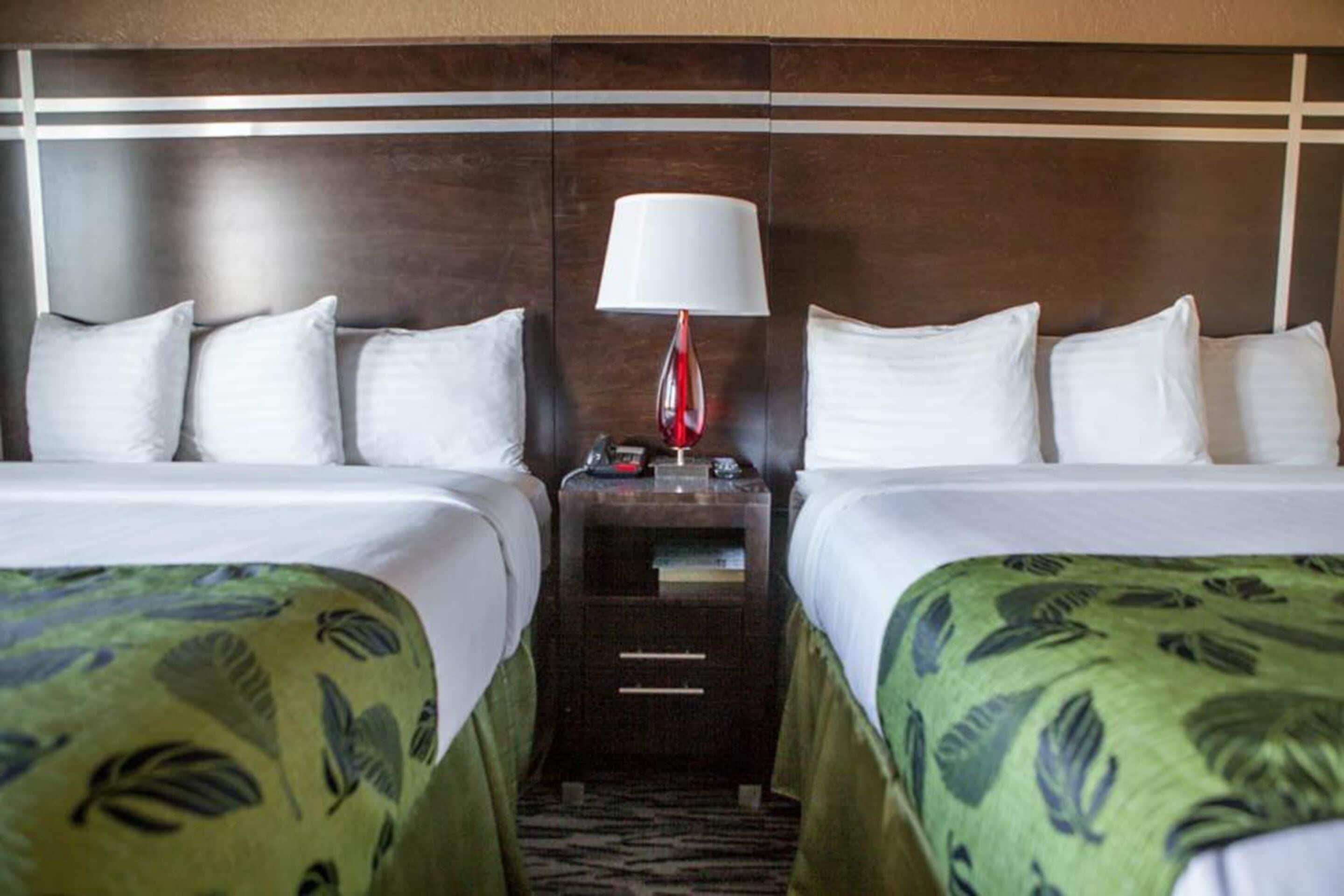 A hotel room with two beds, a nightstand with a lamp, and a patterned bedspread.