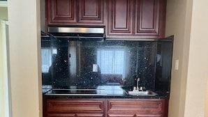 A compact kitchen with dark wooden cabinets, a black countertop, and a stainless steel range hood. - Motel Capri (San Francisco)
