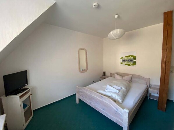 A bedroom with a bed, a television on a stand, a mirror, and a painting on the wall.