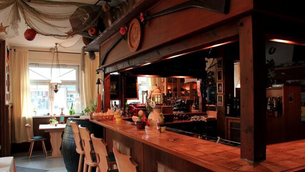 A bar area with wooden bar stools, a large wooden counter, and a variety of bottles and glasses. - Hotel Restaurant Zum Postillion (Soltau)