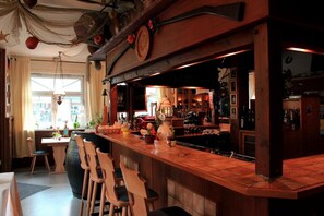 A bar area with wooden bar stools, a large wooden counter, and a variety of bottles and glasses. - Hotel Restaurant Zum Postillion (Soltau)