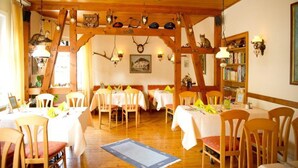 A dining area with wooden beams, tables with white tablecloths, and chairs. - Hotel Restaurant Zum Postillion (Soltau)