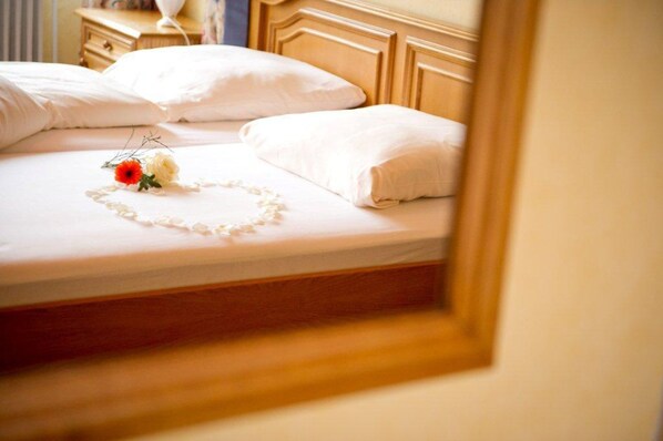 A neatly made bed with white linens and a decorative arrangement of flowers and a string of pearls. - Hotel Restaurant Zum Postillion (Soltau)