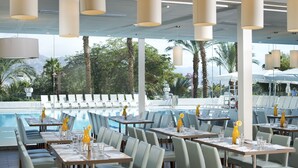 Restaurante com área externa e mesas voltadas para uma piscina, com móveis modernos e iluminação pendente.