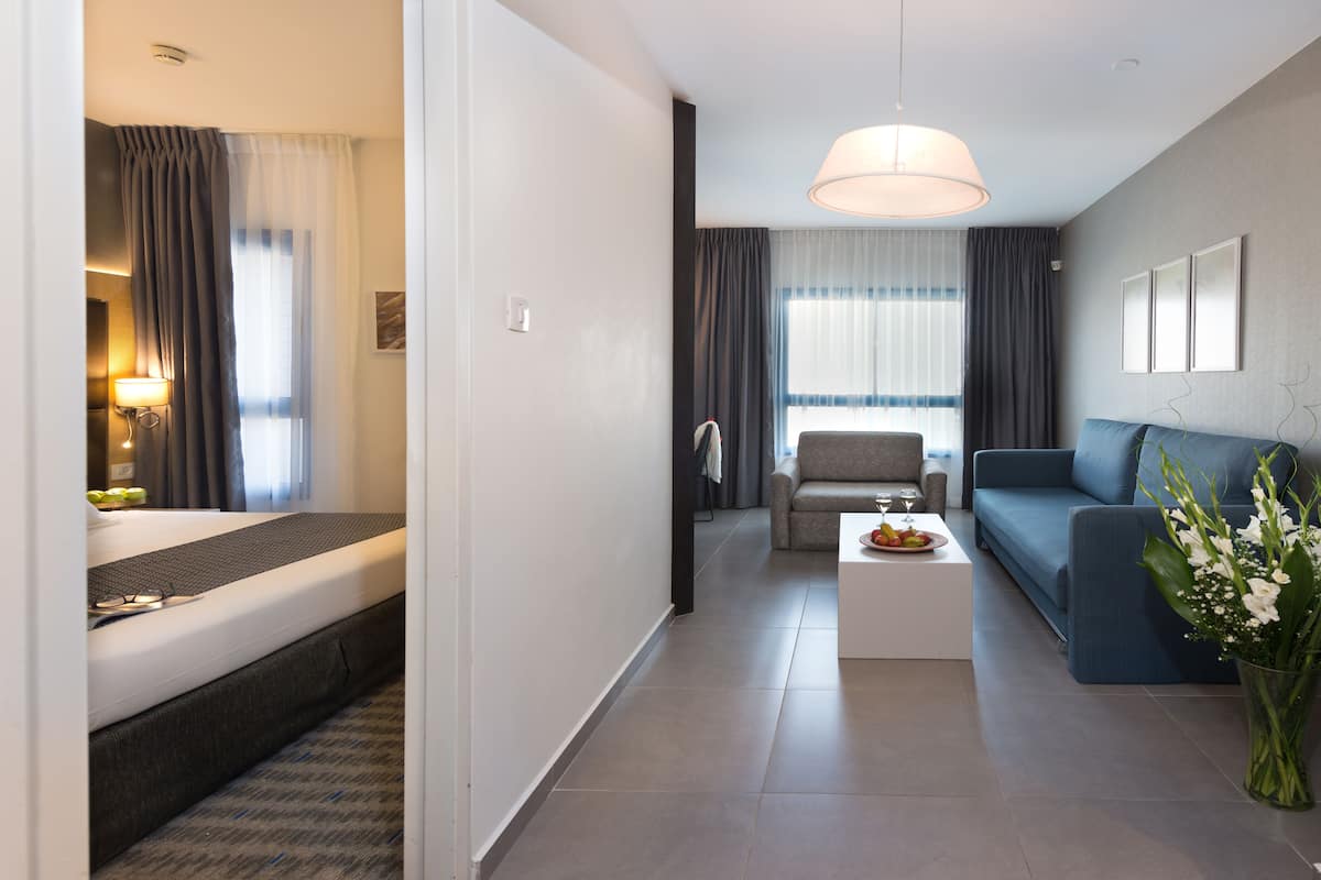 A modern hotel room with a bed, a sofa, a coffee table, and a dining area.