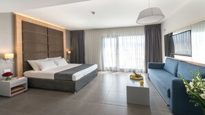 Quarto de hotel moderno com uma cama grande, um sofá, uma TV e uma janela ampla com cortinas.