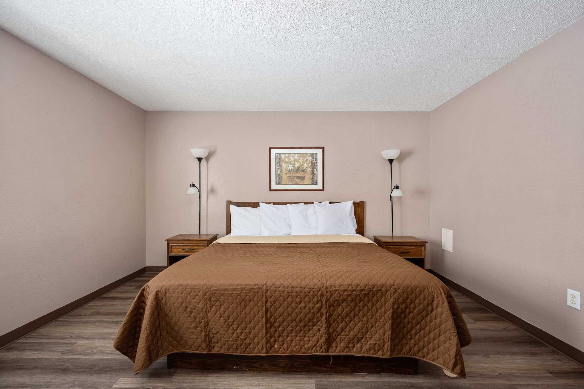 A bedroom with a queen-sized bed, two bedside tables, a nightstand, a framed picture on the wall, and a ceiling light.