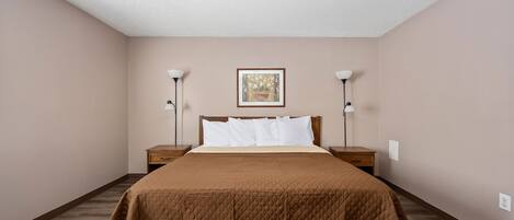A bedroom with a queen-sized bed, two bedside tables, a nightstand, a framed picture on the wall, and a ceiling light.