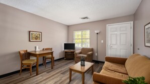 A living room with a wooden floor, a sofa, a TV, a table, and a chair. - Affordable Suites Greenville (Greenville)