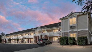 A multi-story hotel with a balcony on the second floor, a parking lot, and a car parked in front. - Affordable Suites Greenville (Greenville)
