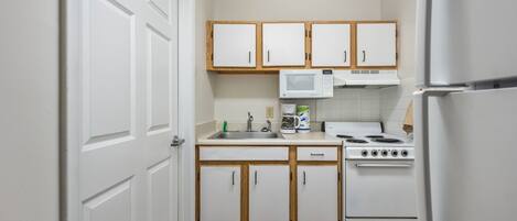 A compact kitchen with white cabinets, a microwave, a stove, and a refrigerator.