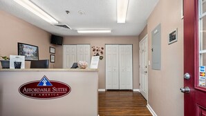 A reception area with a reception desk, a framed picture, a wall-mounted TV, and a door with a lock. - Affordable Suites Greenville (Greenville)