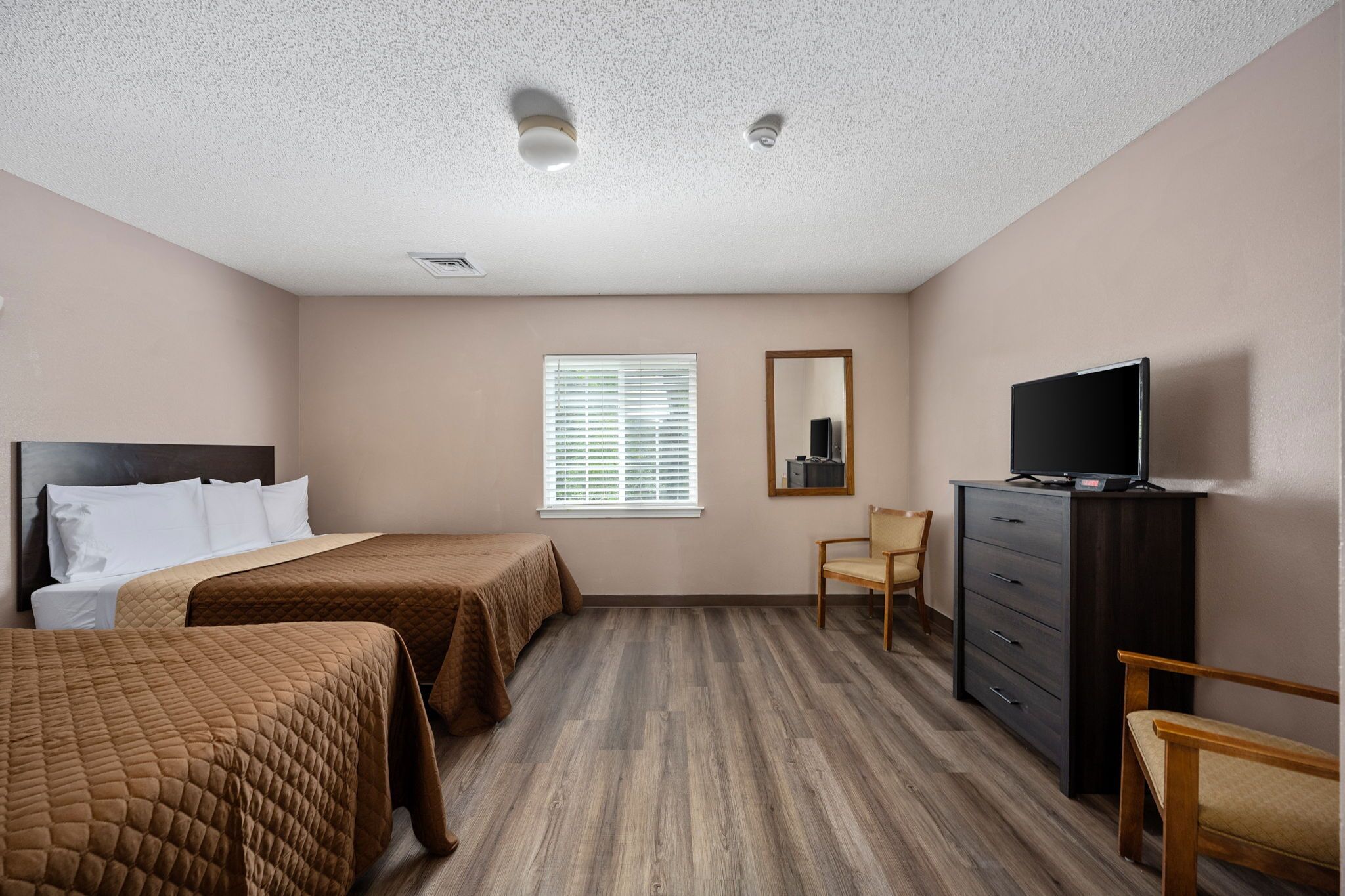 A hotel room with two beds, a dresser, a television, and a window with blinds.