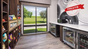 Un mostrador de aperitivos con estantes llenos, una vitrina refrigerada y un amplio ventanal con vistas a un campo cubierto de hierba.