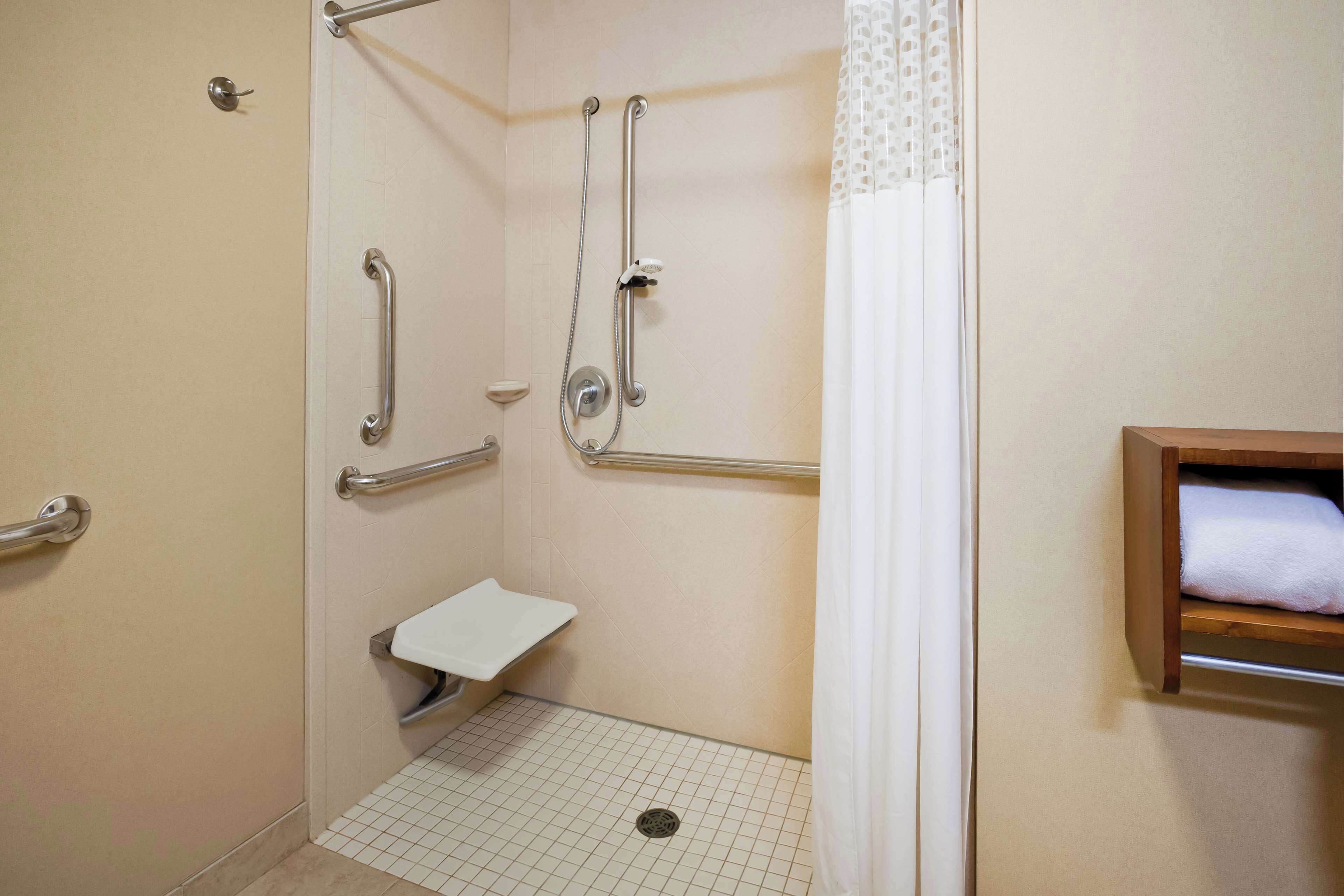 A handicap-accessible shower with grab bars, a white sink, and a towel shelf.