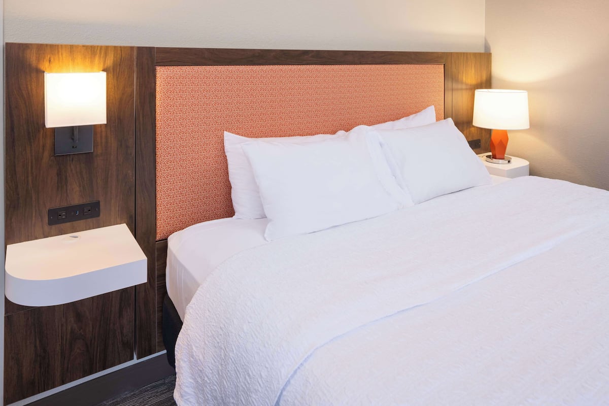 A hotel room with a large bed, two bedside lamps, a nightstand, and a built-in sink.