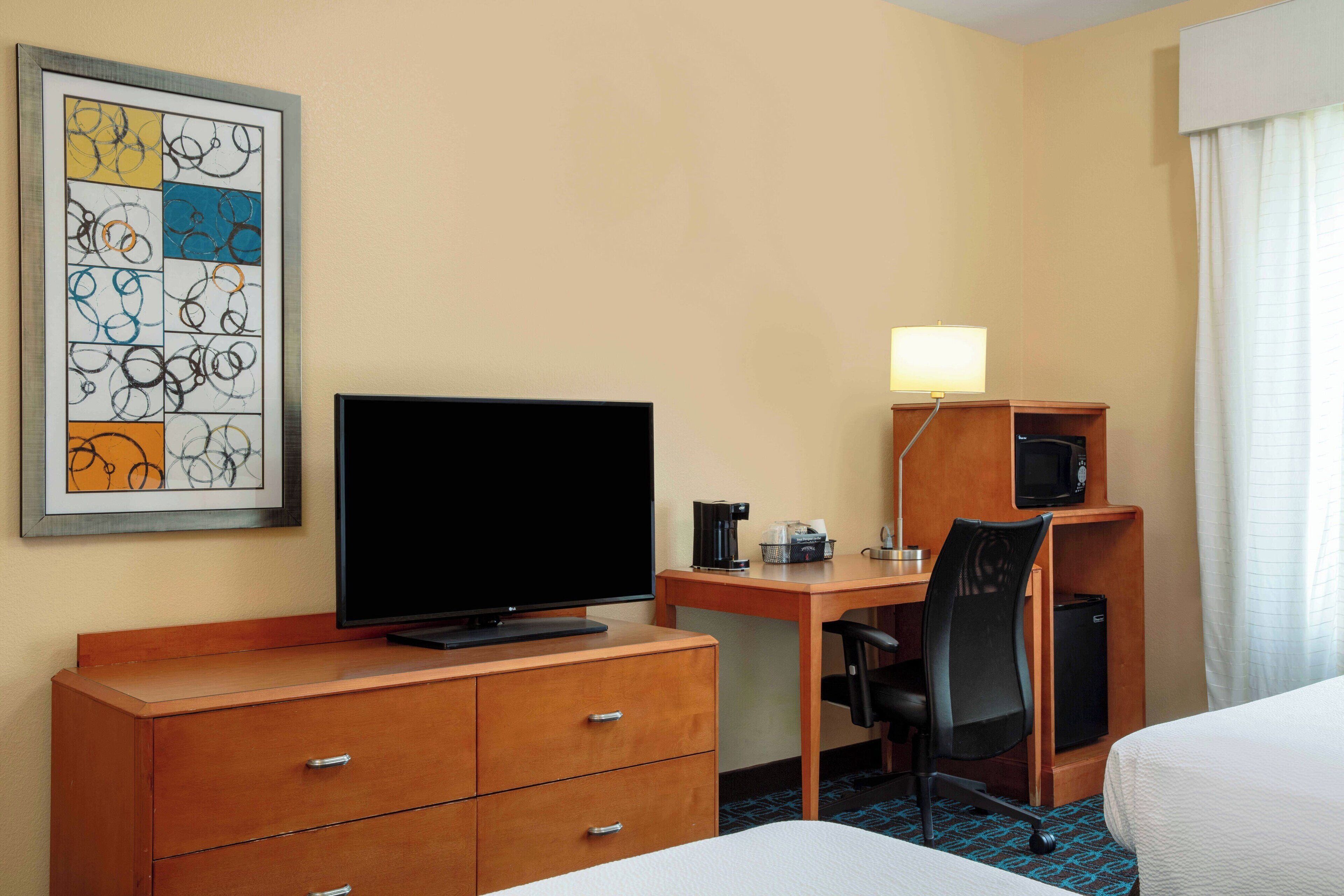 Una habitación de hotel con una cama, un escritorio con computadora, televisión, cafetera y microondas.