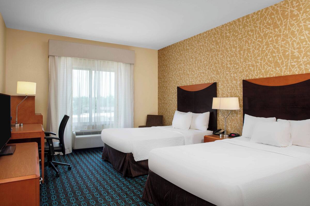 A hotel room with two beds, a desk, a chair, a TV, and a window with curtains.