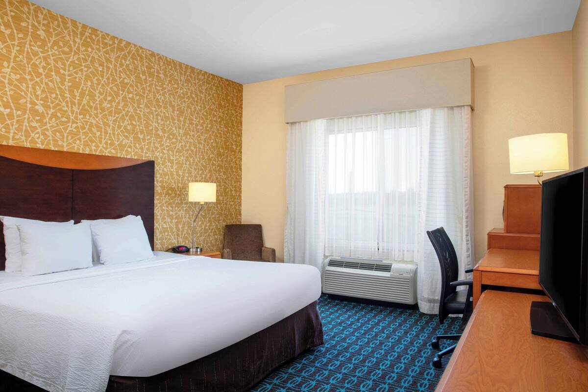 A hotel room with a large bed, a desk with a television, a chair, and a window with curtains.