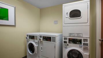 Une buanderie équipée de deux machines à laver superposées et d’un sèche-linge, avec un tableau encadré au mur et un panneau indiquant la durée des cycles de lavage.