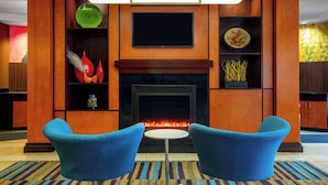 A modern living room with a fireplace, two blue armchairs, and a flat-screen TV above it. - Fairfield by Marriott Inn and Suites Augusta Fort Eisenhower Area (Augusta)