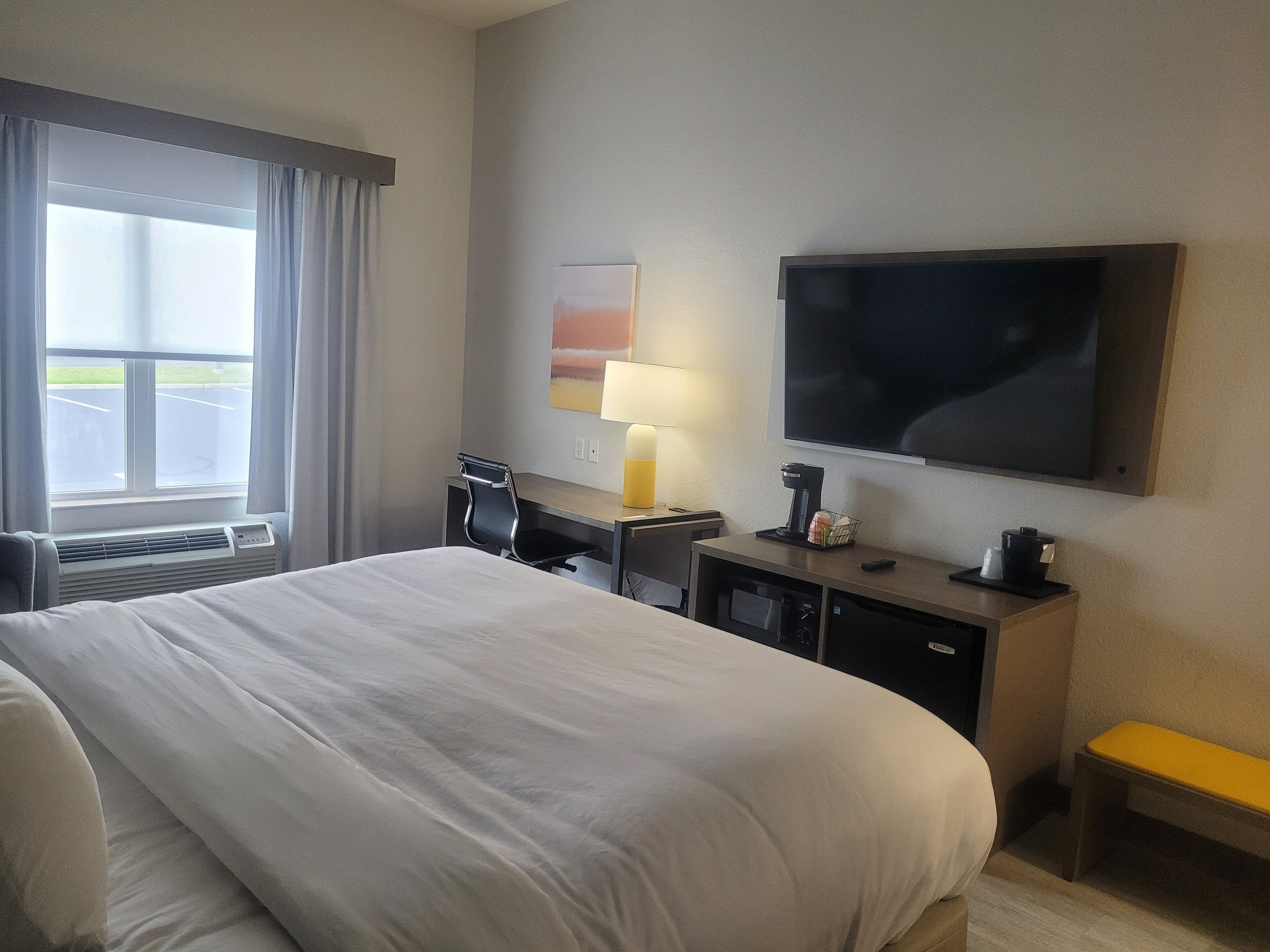 A hotel room with a large bed, a desk with a chair, a television, and a window with curtains.