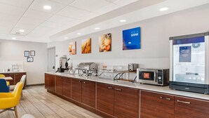 A modern kitchen area with a coffee machine, microwave, and refrigerator, wooden cabinets, and a counter with food items. - Comfort Inn & Suites Dothan Northside Plaza (Dothan)