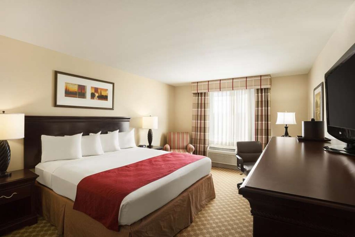 A hotel room with a large bed, a desk, a chair, and a television.