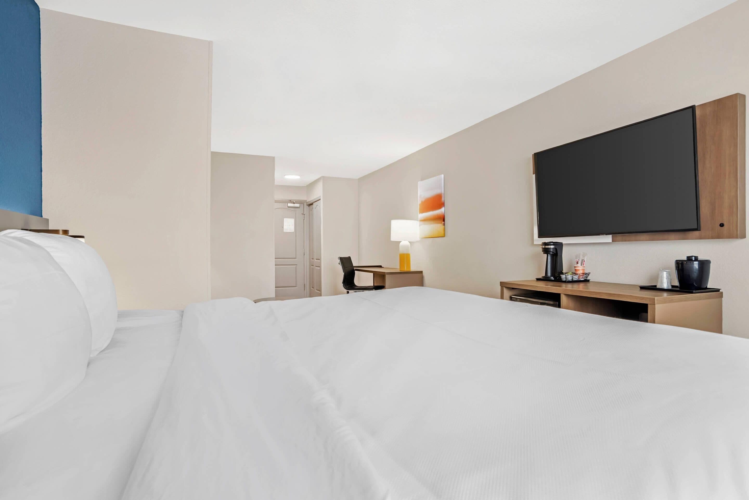 Ein Hotelzimmer mit einem Bett, einem Schreibtisch, einem Stuhl, einem Fernseher und einem Wandbild.