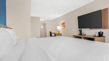 Ein Hotelzimmer mit einem Bett, einem Schreibtisch, einem Stuhl, einem Fernseher und einem Wandbild.