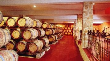 A wine cellar with rows of wooden barrels on shelves and a red carpeted floor.