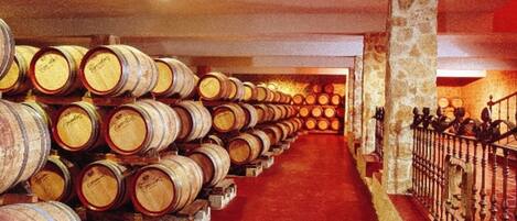 A wine cellar with rows of wooden barrels on shelves and a red carpeted floor.